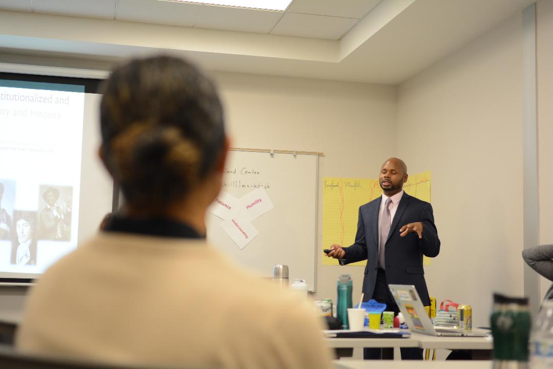Dante King leading a leadership-development session at a whiteboard, a participant seated in the foreground.