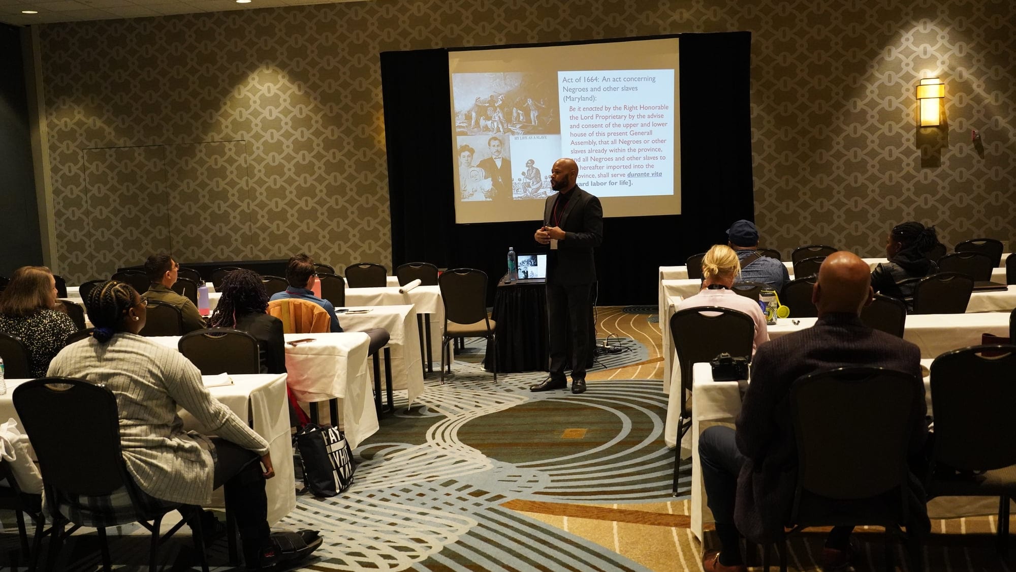 Dante King presenting to a seated audience, a seventeenth-century statute displayed on the screen behind him.