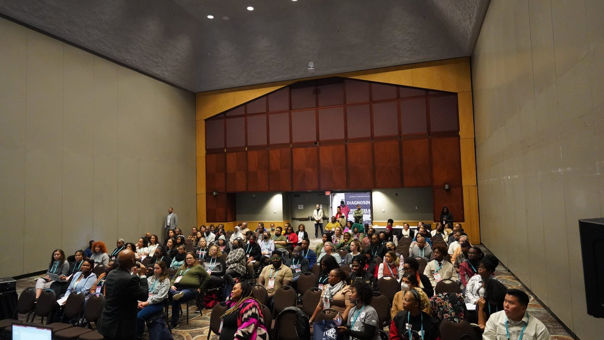 A large room of professionals seated in rows at an institutional training session led by Dante King.